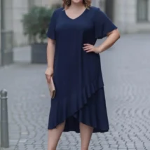 Sukienka Fari: przód sukienki z dekoltem V i falbaną, ujęcie z boku, z ręką na biodrze.