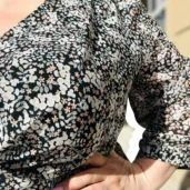 Lili sukienka asymetryczna: detal dekoltu i rękawa 3/4, widoczny drobny, kwiatowy wzór na czarnym tle.