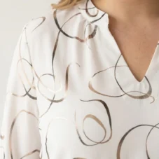 Biała elegancka bluzka w złote abstrakcyjne wzory, zbliżenie na dekolt w serek i stójkę.