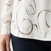 Biała elegancka bluzka w złote abstrakcyjne wzory, zbliżenie na mankiet i dół bluzki.