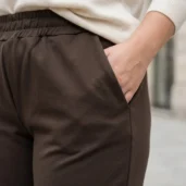 Spodnie brązowe z grubszej dzianiny. Zbliżenie na boczny panel, elastyczny pas i praktyczną kieszeń.