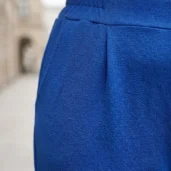 Spodnie na gumce z kieszeniami i z mankietem: zbliżenie na elastyczny pas i detal plisy z przodu.
