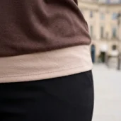 Brązowa bluzka damska z motywem pióra, detal beżowego ściągacza na dole i boczny układ materiału.