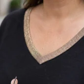 Bluzka z motywem geometrycznych linii, zbliżenie na dekolt V-kształtny z błyszczącą lamówką.