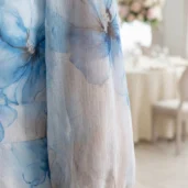 Szyfonowa sukienka plus size wizytowa w błękitne kwiaty, detal długiego, transparentnego rękawa.