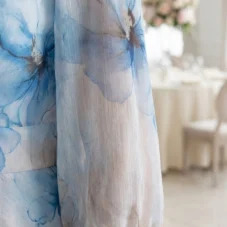 Szyfonowa sukienka plus size wizytowa w błękitne kwiaty, detal długiego, transparentnego rękawa.